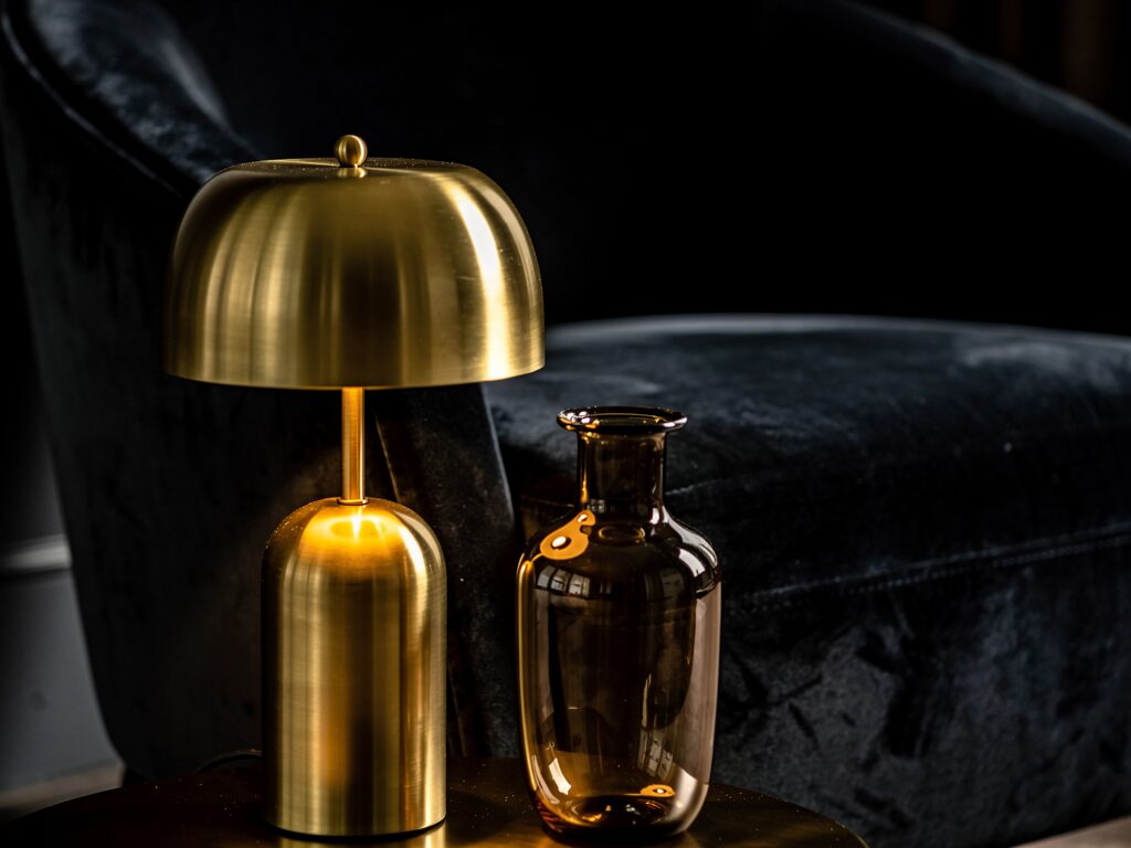 マットな暗い色のソファに対して、光を反射する真鍮のテーブルランプやガラスの花瓶を配置し、暗さを回避した異素材ミックスのインテリア